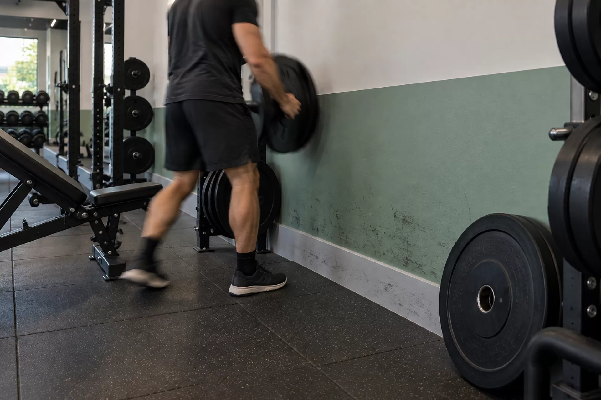 Pessoa apoiando anilha na parede da academia, na altura em que o peso encosta