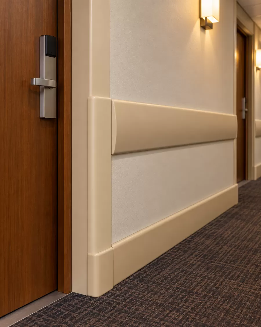 Detalhe do perfil de proteção instalado na parede do corredor de hotel, junto à porta do apartamento
