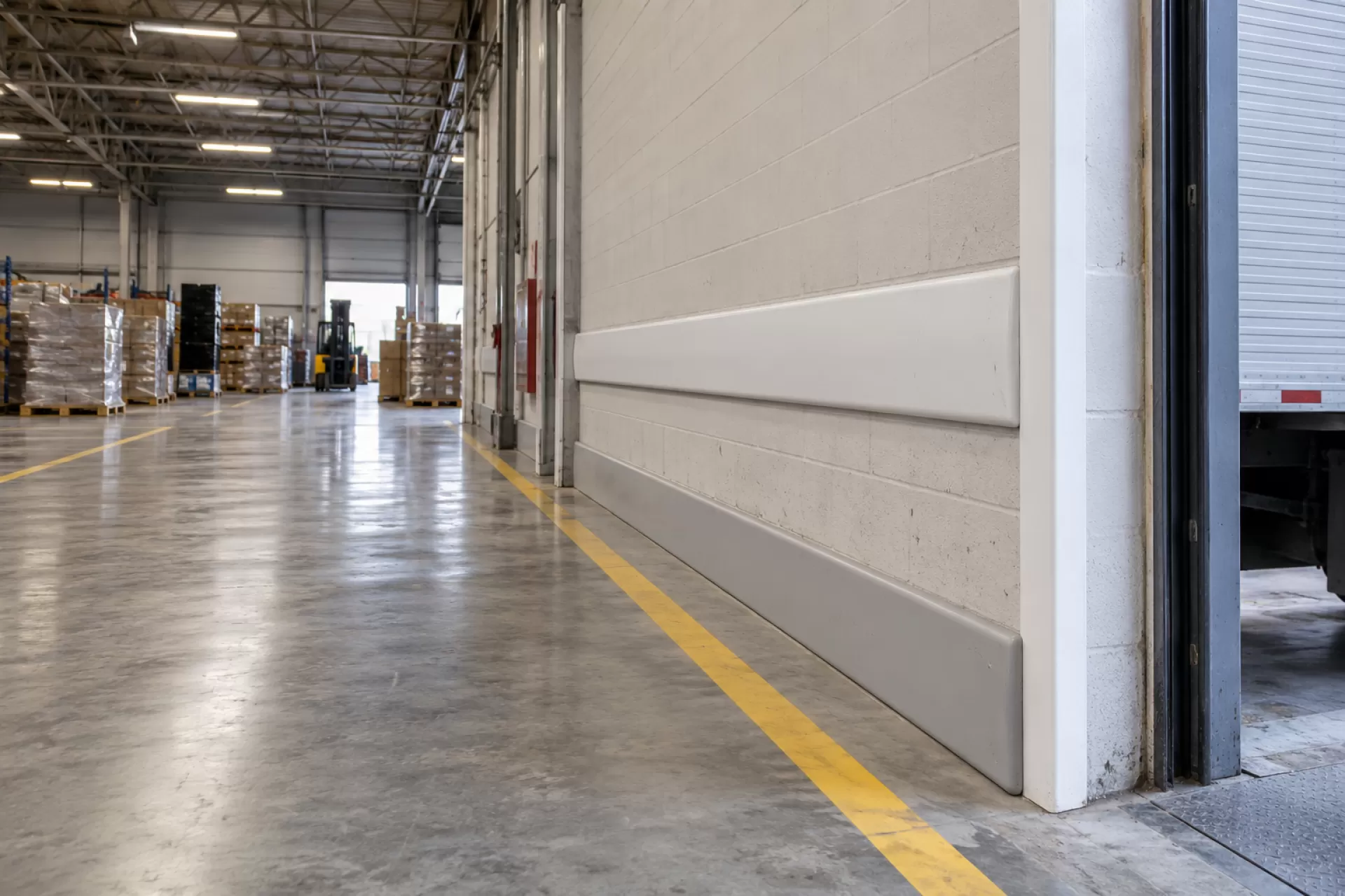 Corredor de galpão industrial com faixa de circulação no piso e proteção de parede instalada